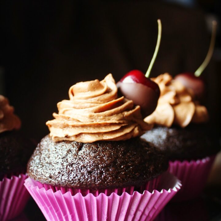 Three espresso chocolate cupcakes with frosting and cherries.