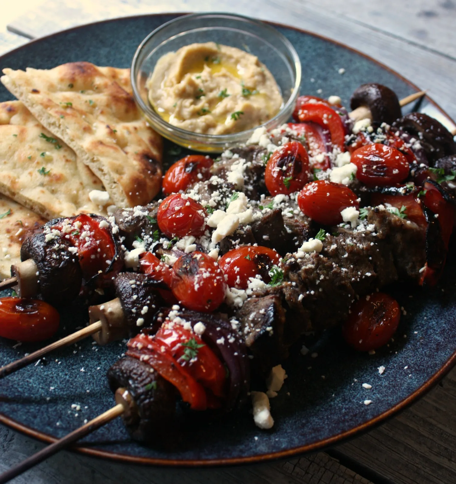 Beef Kabobs with Blistered Tomatoes and Feta Cheese. Served with grilled naan bread and a side of hummus. 