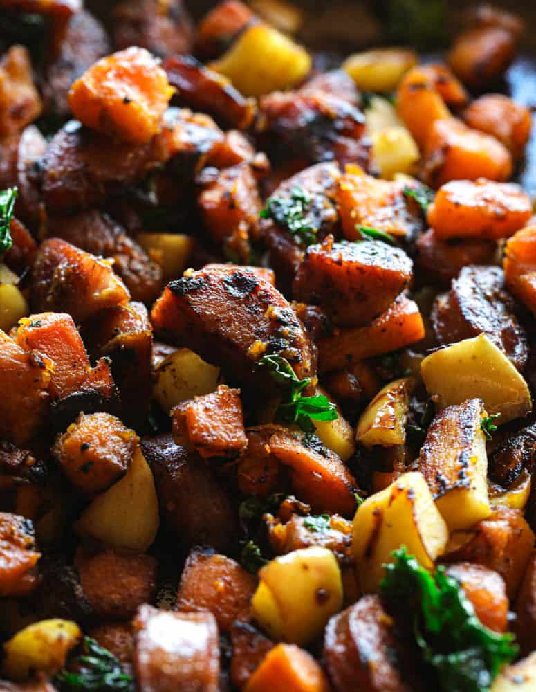 Sweet potato hash closeup, with pieces of apple, chicken sausage, and kale. All cooked together in a skillet on the stove.
