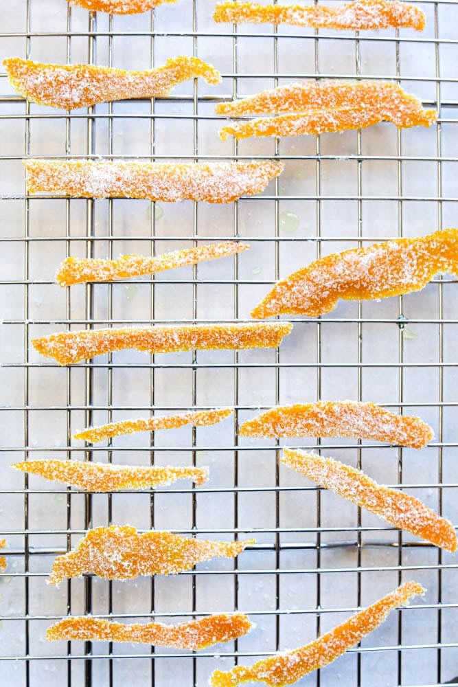 Orange candied peels coated in sugar on a wire rack.