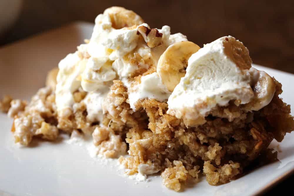 Heaping scoop of baked banana oatmeal on a plate topped with whipped cream, banana slices, and pecans