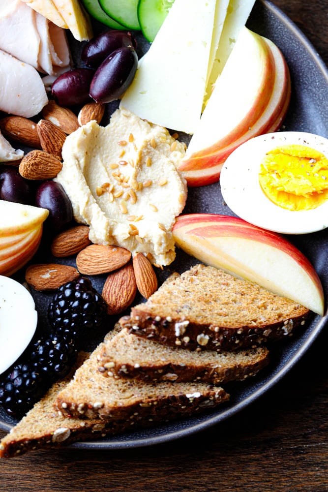 High protein lunch board with turkey, hummus, fresh vegetables, berries, and hard boiled egg