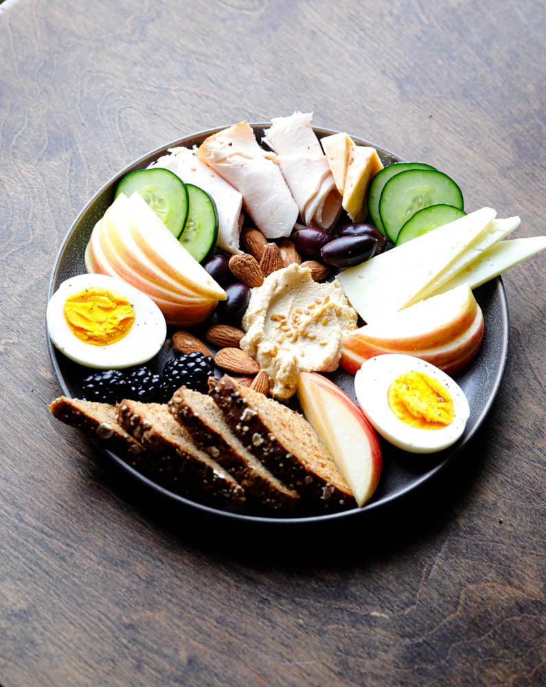 Easy high protein snack board with turkey, cheese, hummus, olives, cucumbers, and berries