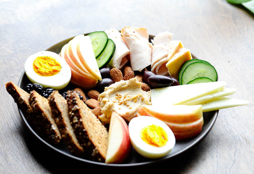 Healthy high protein comfort food snack board with turkey slices, fruit, nuts, and hummus