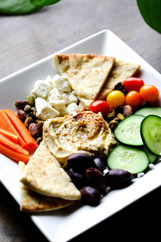 Mediterranean snack board with hummus, feta, cucumbers, olives, pistachios, and fresh vegetables