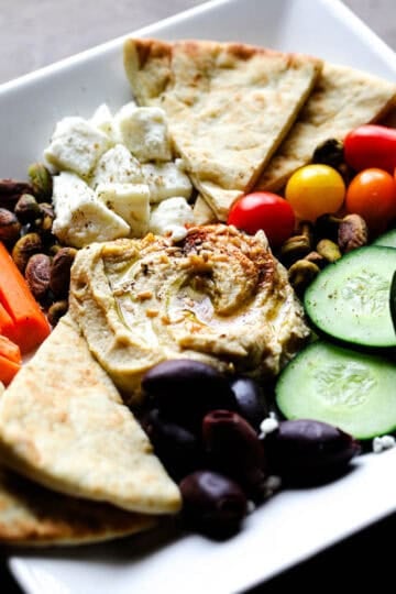 Mediterranean hummus snack plate with feta cheese, olives, cucumbers, tomatoes, pistachios, and pita bread