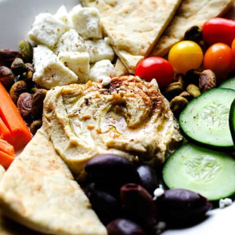 Mediterranean hummus snack plate with feta cheese, olives, cucumbers, tomatoes, pistachios, and pita bread