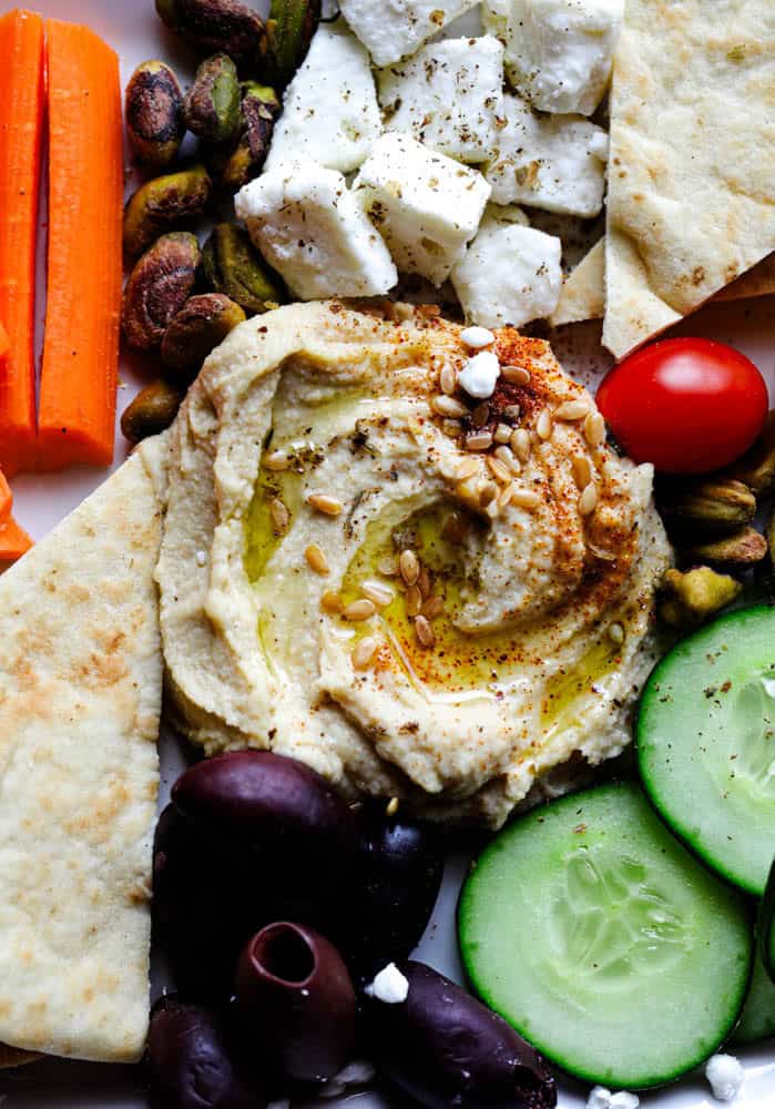Close-up of creamy hummus with olive oil, feta cheese, olives, cucumbers, and pita bread on a Mediterranean snack plate